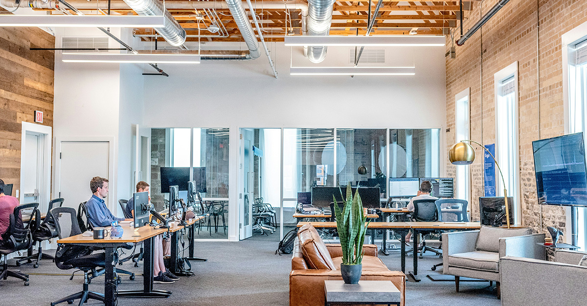 Open space lumineux avec bureaux, fauteuils, plantes et grande baie vitrée