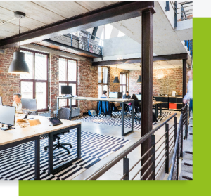 Open space lumineux avec murs en briques, grandes fenêtres et bureaux partagés dans un style industriel