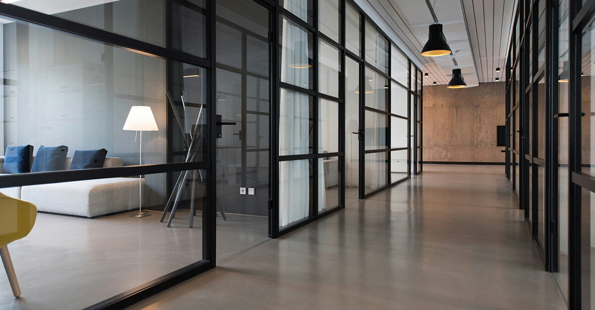 Couloir lumineux avec cloisons vitrées, portes noires et mobilier contemporain