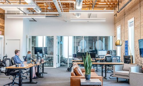 Open space lumineux avec bureaux, fauteuils, plantes et grande baie vitrée