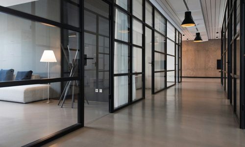 Couloir lumineux avec cloisons vitrées, portes noires et mobilier contemporain